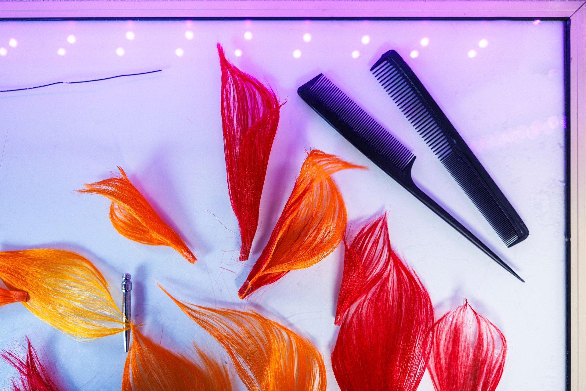 Colorful hair extensions with styling combs. Bright red and orange hairpieces on light background.